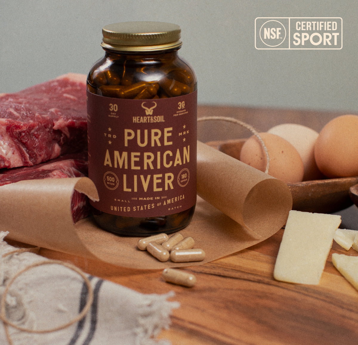 Bottle of 'Pure American Liver' supplements on a wooden surface with raw meat, eggs, and cheese.