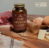 Bottle of 'Pure American Liver' supplements on a wooden surface with raw meat, eggs, and cheese.