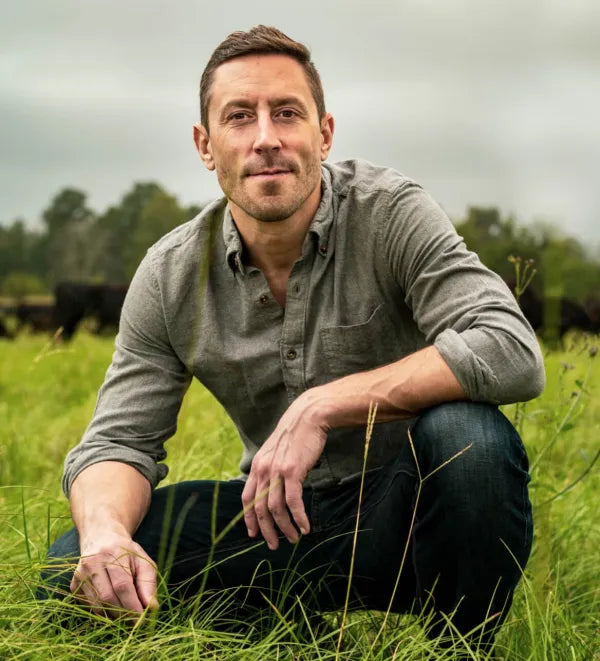 Paul Saladino kneeling in a green pasture