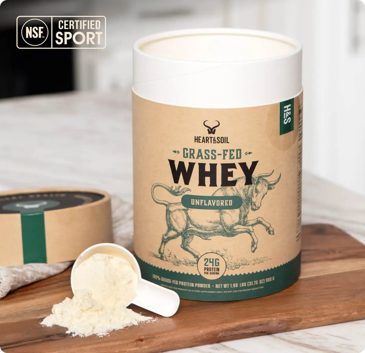 Container of grass-fed whey protein powder with a scoop of powder on a wooden surface.